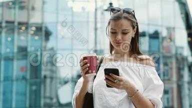 微笑可爱的女人带着一杯咖啡在商业街使用手机